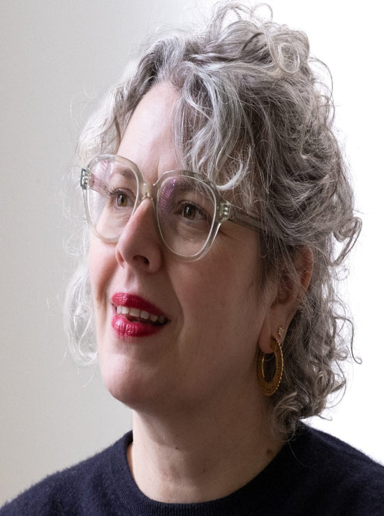 Person with gray hair wearing glasses and a dark sweater against a plain background